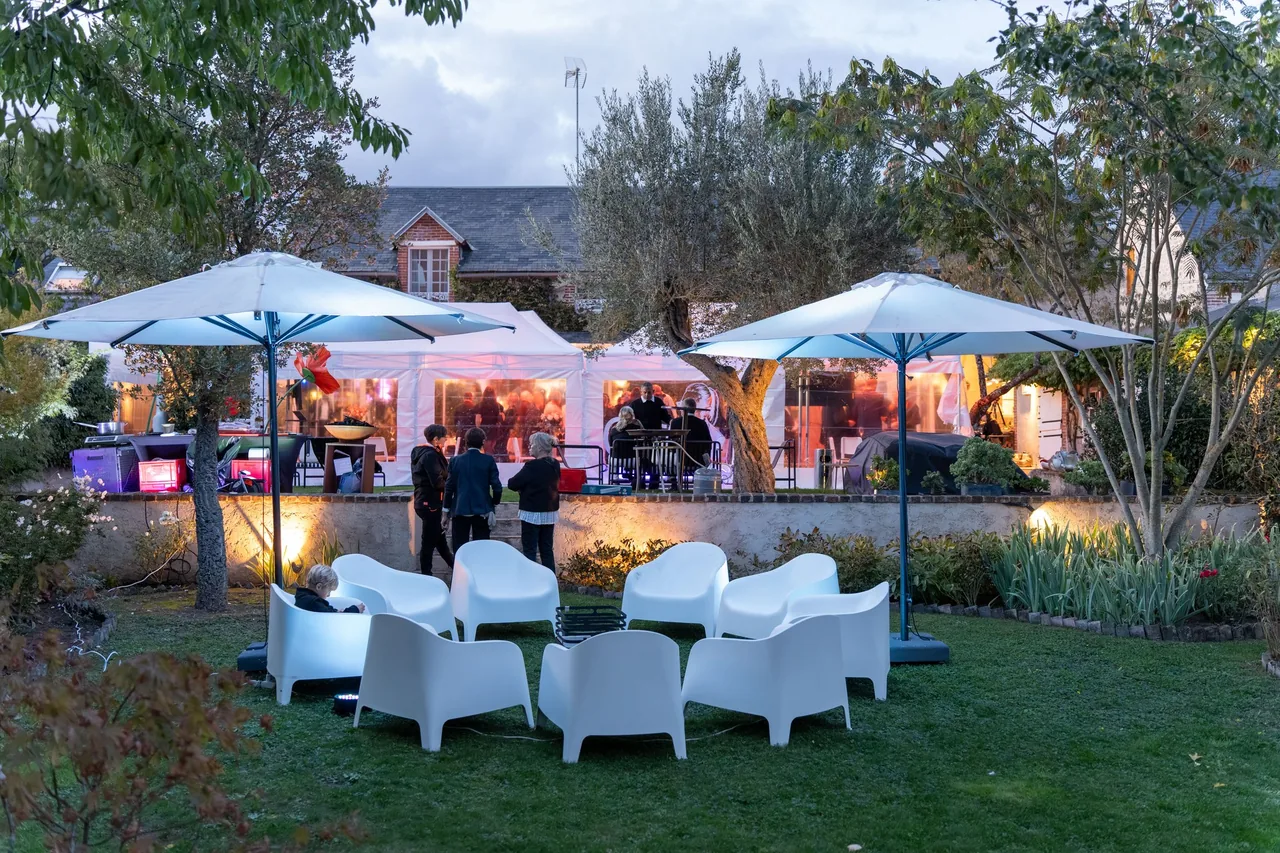 Der Garten des Festes zu Mémés 100. Geburtstag in der Abenddämmerung: weiße Zelte, Sonnenschirme und weiße Loungesessel vor dem Haus, im Tal des Loir