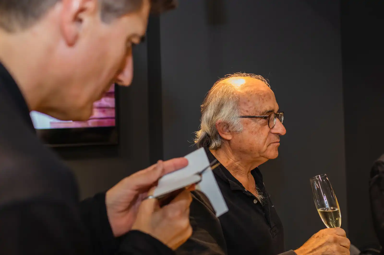 Ein Gast hält ein Glas Champagner, während Igor Kucinic bei einem Cocktailempfang ein Scherenschnittporträt schneidet