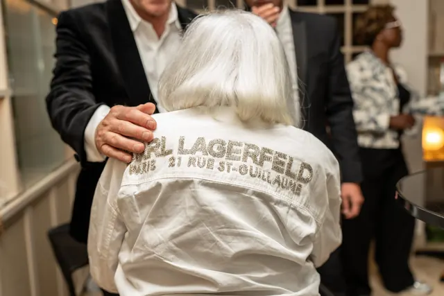 Mémé von hinten in ihrem weißen Karl-Lagerfeld-Hemd, von einem Gast umarmt